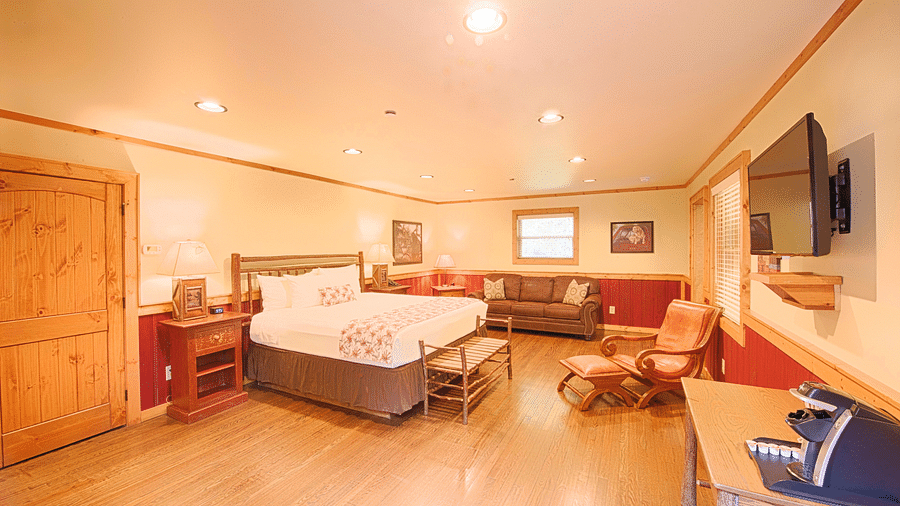 a cushioned armchair placed opposite to the double bed in the room with a closed wooden door besides it - Historic Tapoco Lodge