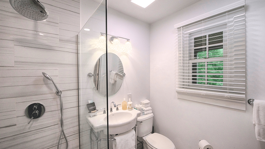 a bathroom with a wash basin along with a wall mounted circular mirror and a commode beside it with a small window for ventilation - Historic Tapoco Lodge