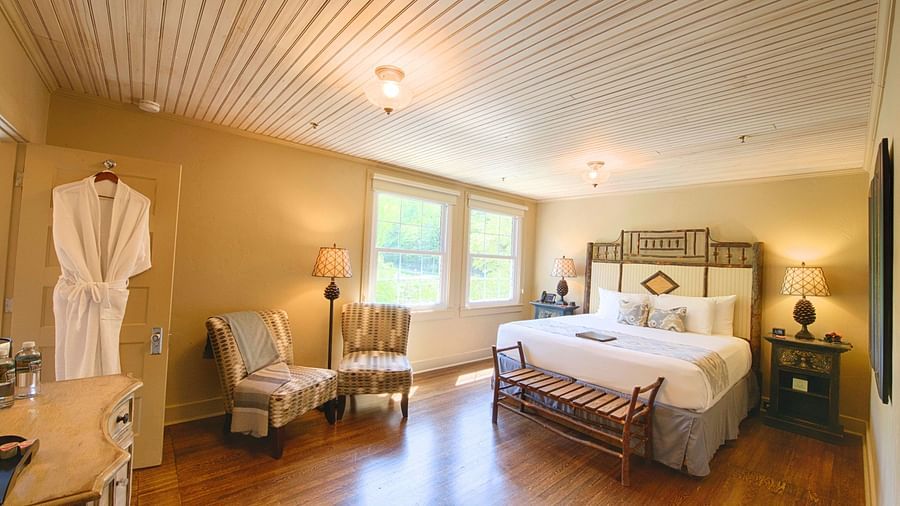 full view image of a bedroom with a plush double bed with a beautiful headboard and a bathrobe hanging on the bathroom door - Historic Tapoco Lodge