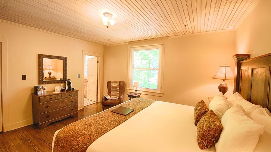 corner view image of a bedroom featuring a plush soft double bed with a small window in the far end of the room - Historic Tapoco Lodge
