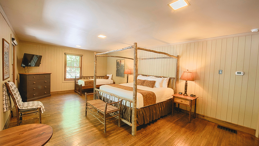 corner view image of a room with a double bed surrounded by four wooden pillars bed side tables - Historic Tapoco Lodge