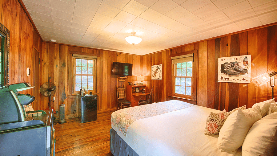 a bedroom with wooden interiors with two windows and a wall mounted television placed opposite to the double bed - Historic Tapoco Lodge
