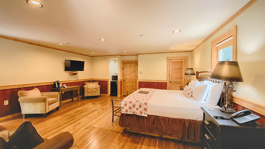 a plush double bed with a lamp placed on a bed side table along with a wall mounted television in the corner - Historic Tapoco Lodge
