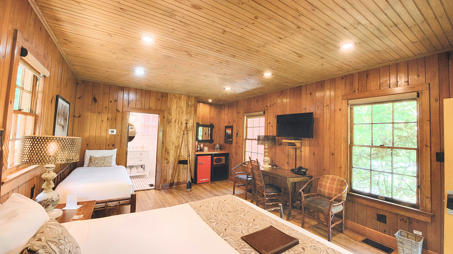 a bedroom overlooking a double bed with a file kept on it facing towards a window with lush green views outside - Historic Tapoco Lodge