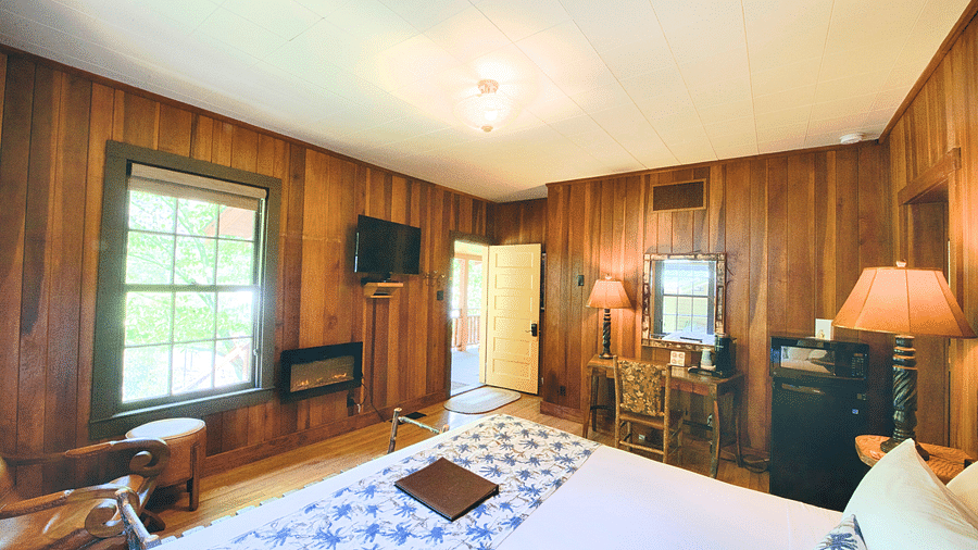 a cozy room featuring wooden interiors overlooking a double bed, a writing desk along with a vintage inspired decor - Historic Tapoco Lodge