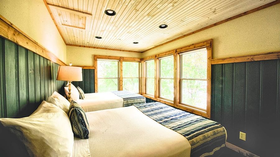 a cozy bedroom with two beds and a wooden ceiling along with huge five panel window - Historic Tapoco Lodge