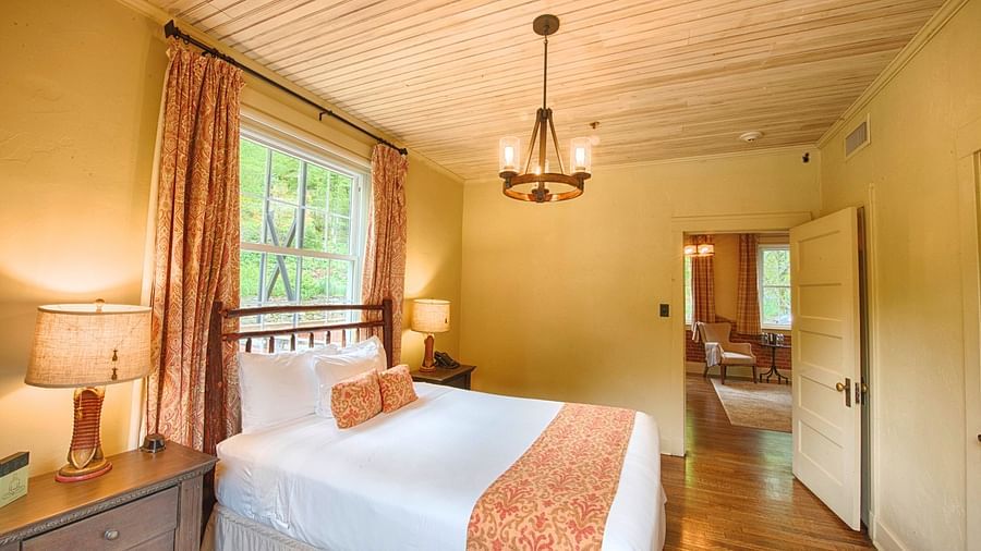 side view image of a double bed right under the chandelier with a window behind the bed - Historic Tapoco Lodge