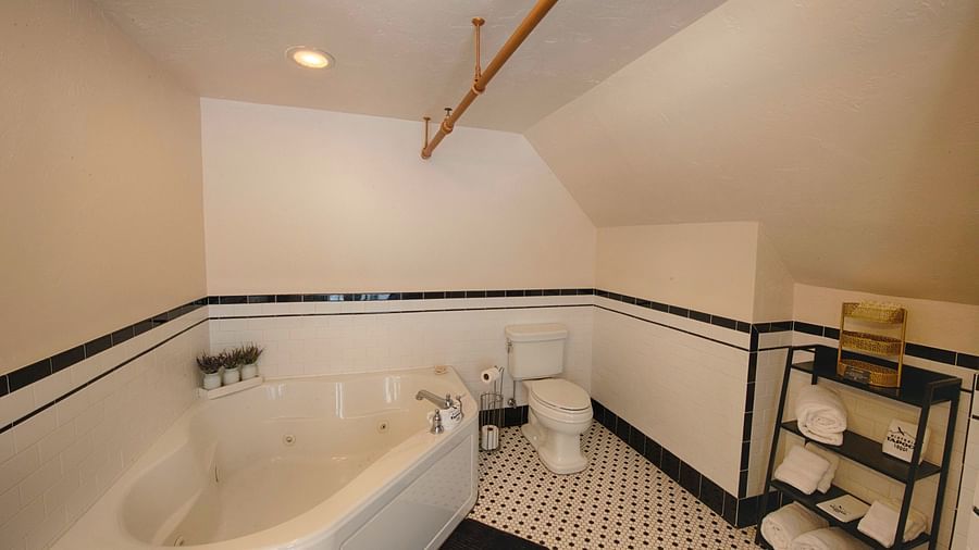 full view image of the bathroom featuring a bathtub along with a commode and a small utility rack in the corner - Historic Tapoco Lodge