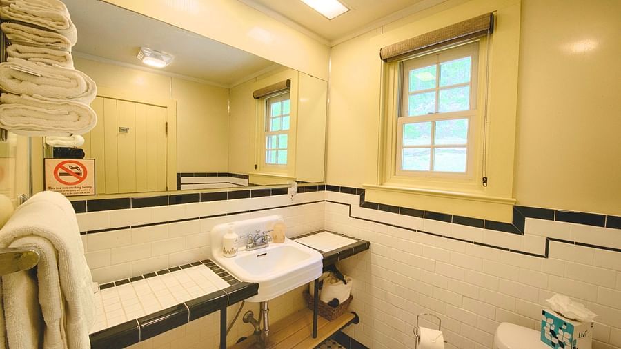 a wash basin with a wide mirror above it and a small closed window beside it in a bathroom - Historic Tapoco Lodge