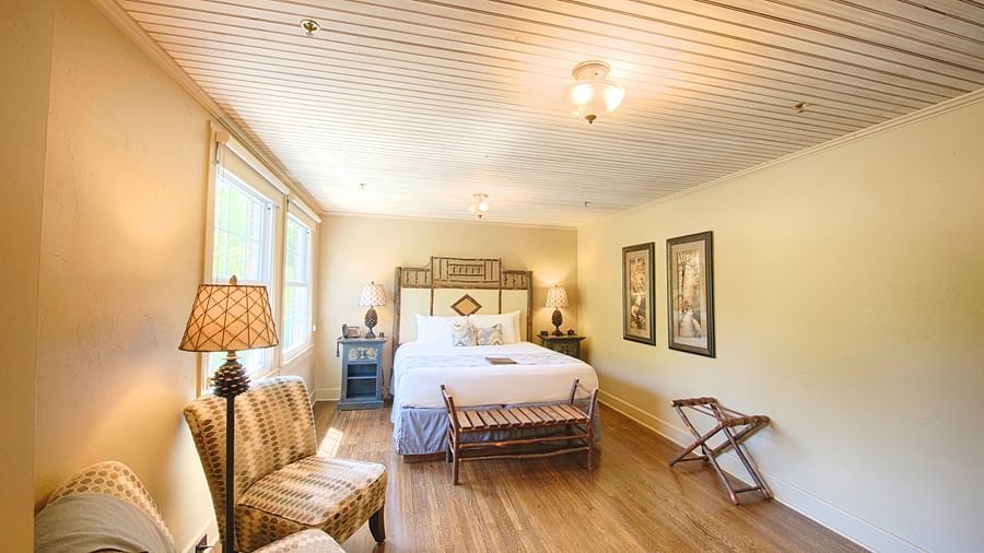 full view image of a bedroom with modern furnishings featuring a double bed along with two cushioned armchairs - Historic Tapoco Lodge