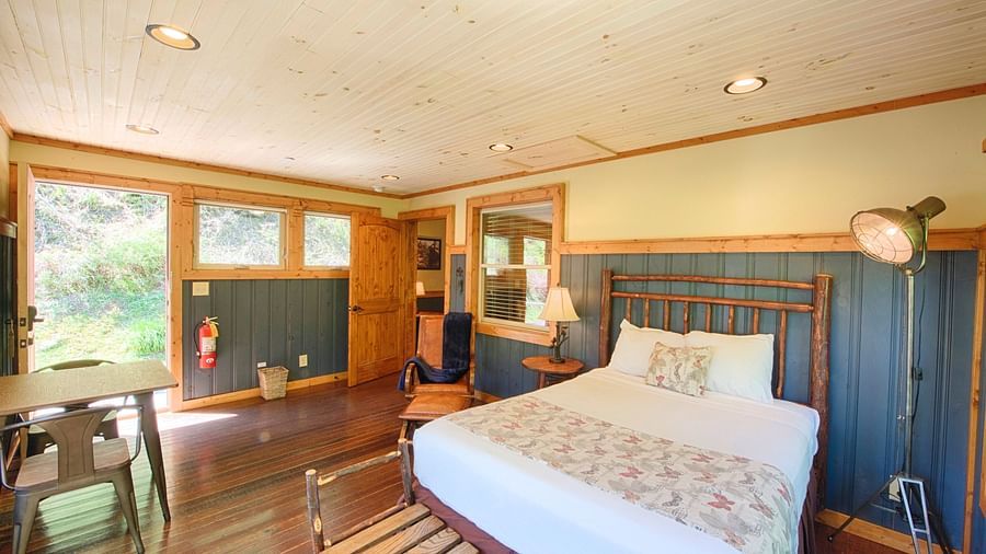 front view image of a bedroom with vibrant interiors and wooden flooring featuring a double bed with a vintage tall lamp besides it -Historic Tapoco Lodge