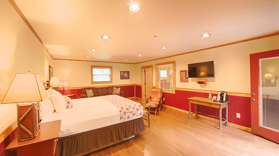 corner view image of a room featuring a double bed placed right opposite to a flat screen wall mounted television - Historic Tapoco Lodge