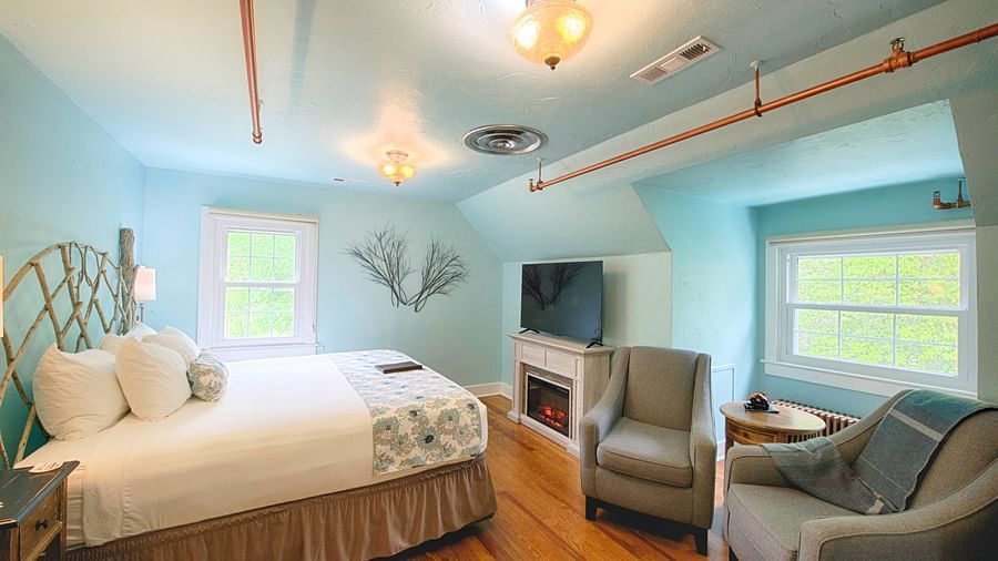 full view image of the laurel suite with pastel blue colored walls along with a flat screen television right opposite to the double bed - Historic Tapoco Lodge