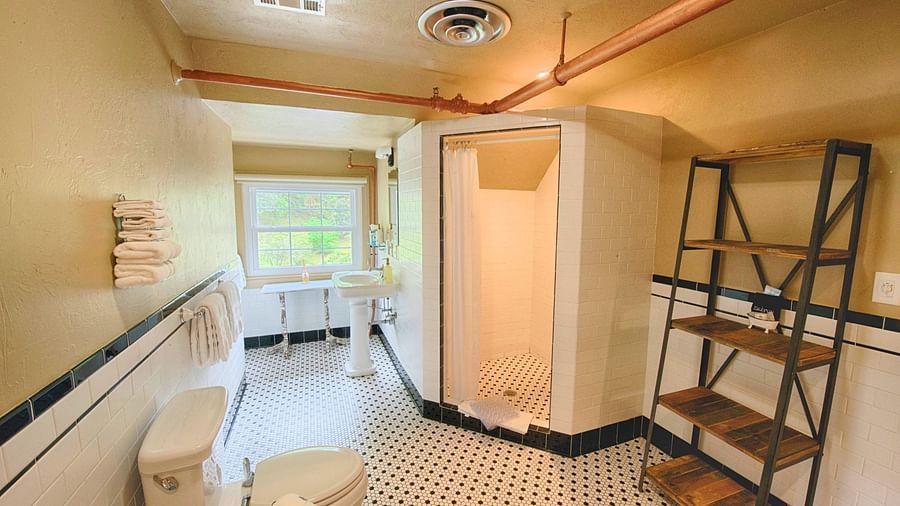 full view image of a bathroom with a shower cubical along with a wooden shelf and a commode - Historic Tapoco Lodge