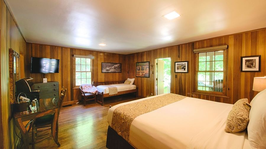 corner view image of a bedroom decorated with small photo frames on the wooden wall with a double and a single bed in the room - Historic Tapoco Lodge