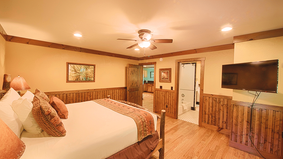 side view image of a bedroom with a double bed along with a wall mounted television in front of it - Historic Tapoco Lodge