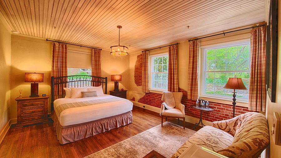 a room with ample natural lighting coming from the huge windows in the room with plush arm chairsa brightly lit bathroom featuring a door opening to the bedroom overlooking the double bed - Historic Tapoco Lodge