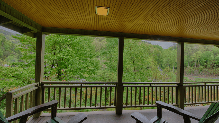 a beautiful wooden porch featuring two chairs facing towards the lush green forest views - Historic Tapoco Lodge