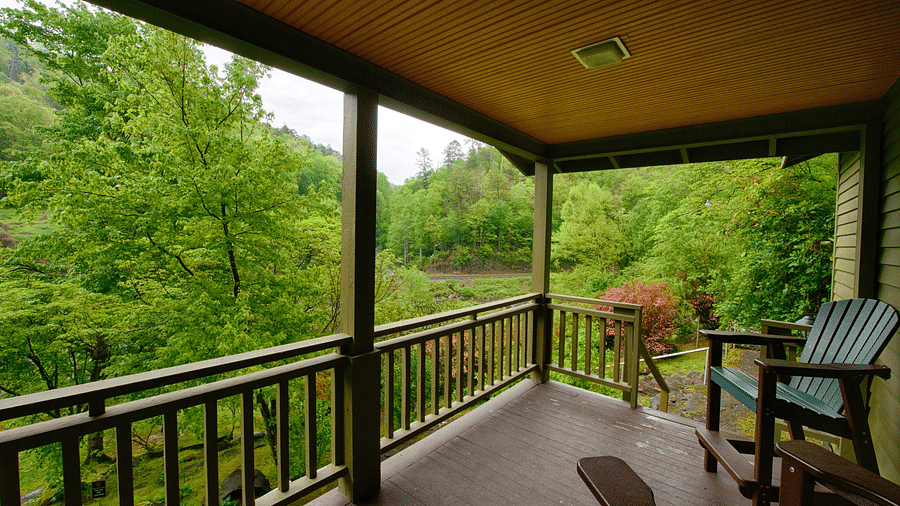 side view of a porch with wooden chairs placed on it overlooking the lush green scenic views - Historic Tapoco Lodge