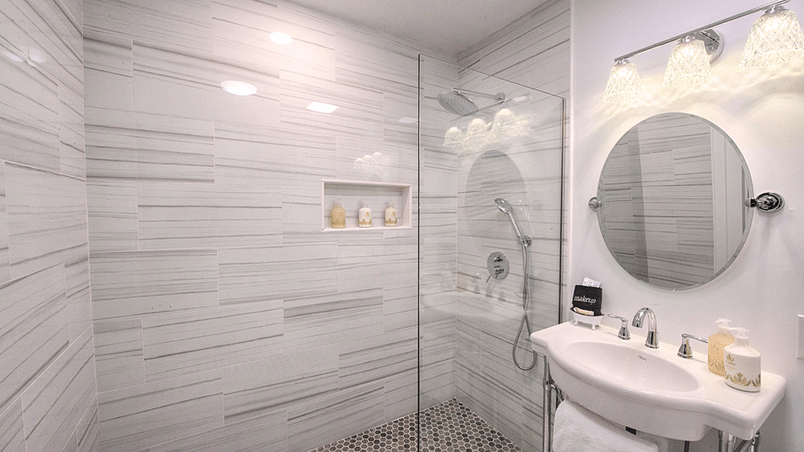 a bathroom with grey gradient tiles with a separate shower area and a circular shaped mirror - Historic Tapoco Lodge