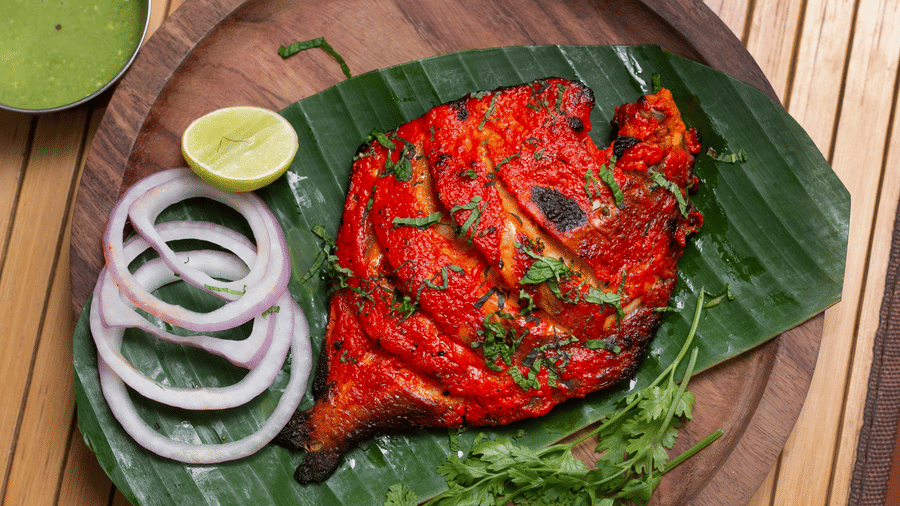 Grilled fish served on a banana leaf with lime, sliced onions, and chutney on a wooden plate at Paradise Lagoon Resort, Udupi.