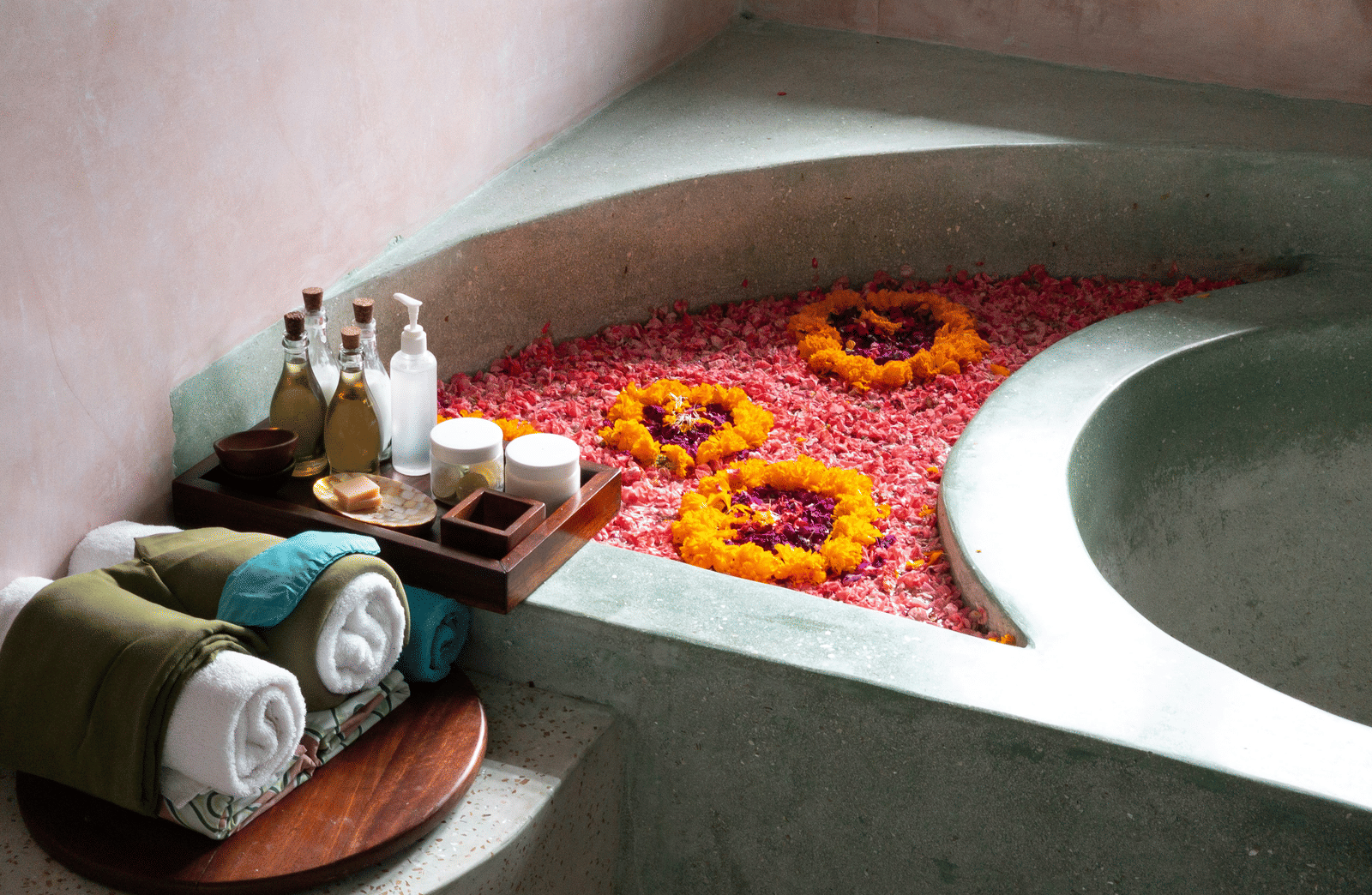 A stone bath filled with water and vibrant flower petals, surrounded by spa amenities.