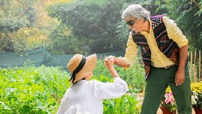 Staff member serving food to a seated guest in the garden area of Karma Chalets during daylight.