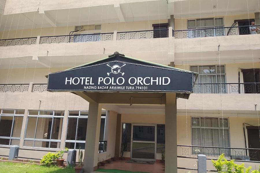 alt-text The entrance of Hotel Polo Orchid with its name on the signboard, and part of the building's beige facade.