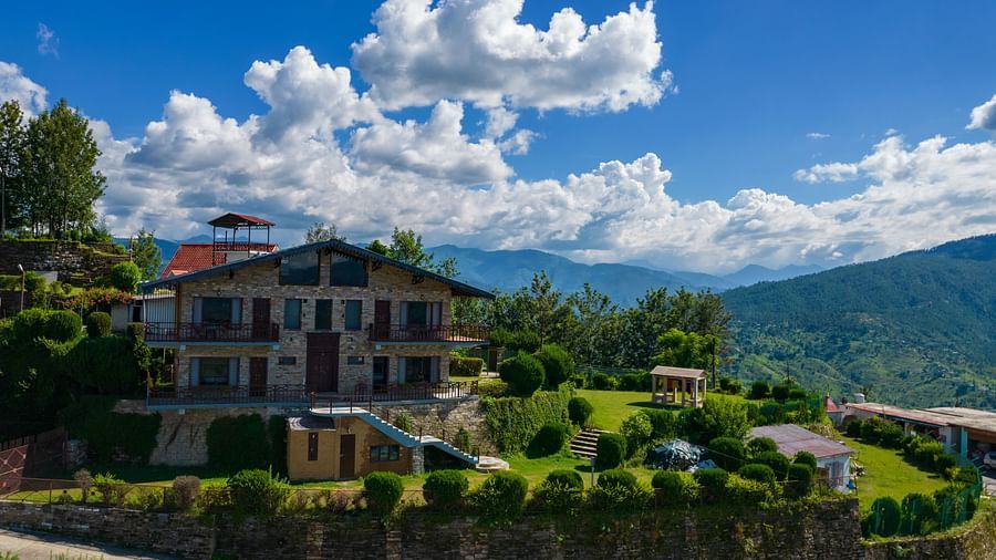 A charming villa surrounded by lush greenery and set against the backdrop of rolling hills and blue skies. - Blusalzz Homes The Himalayan Bungalow, Almora