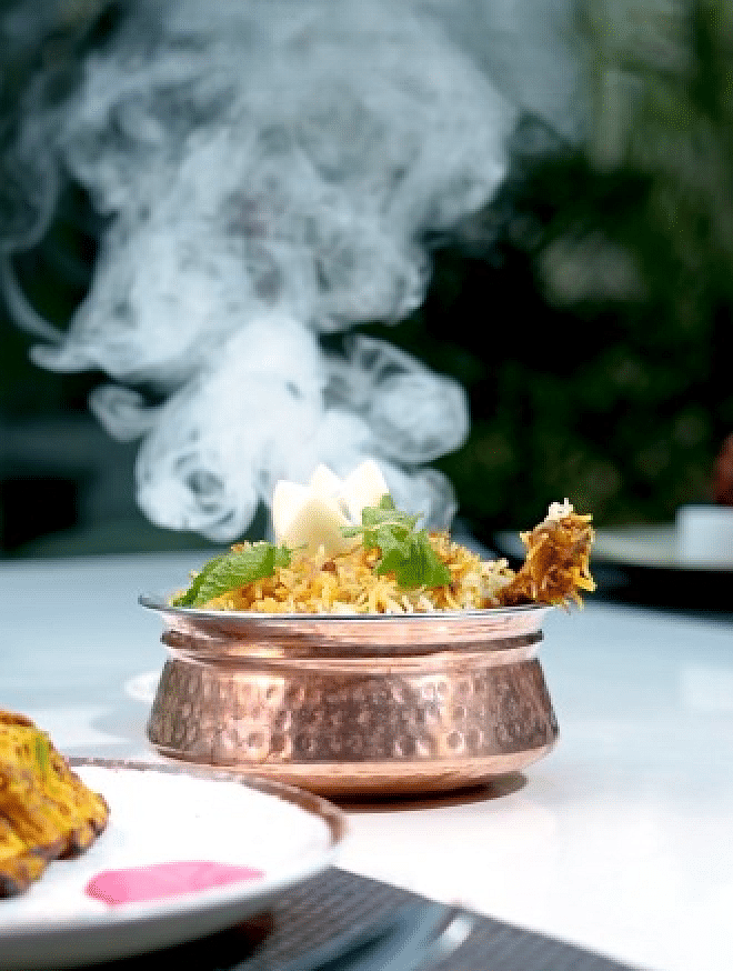 A steaming dish in a copper pot, with smoke rising and a blurred background at Cenneys Gateway.