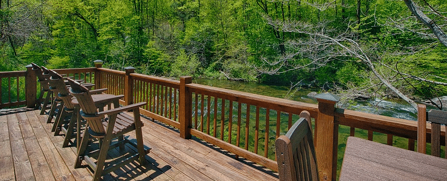 a wooden porch protected by hand railings with several wooden chairs lined up facing towards the forest - Historic Tapoco Lodge