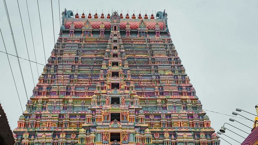 A majestic temple gopuram towers upwards, adorned with colourful sculptures and flanked by power lines.
