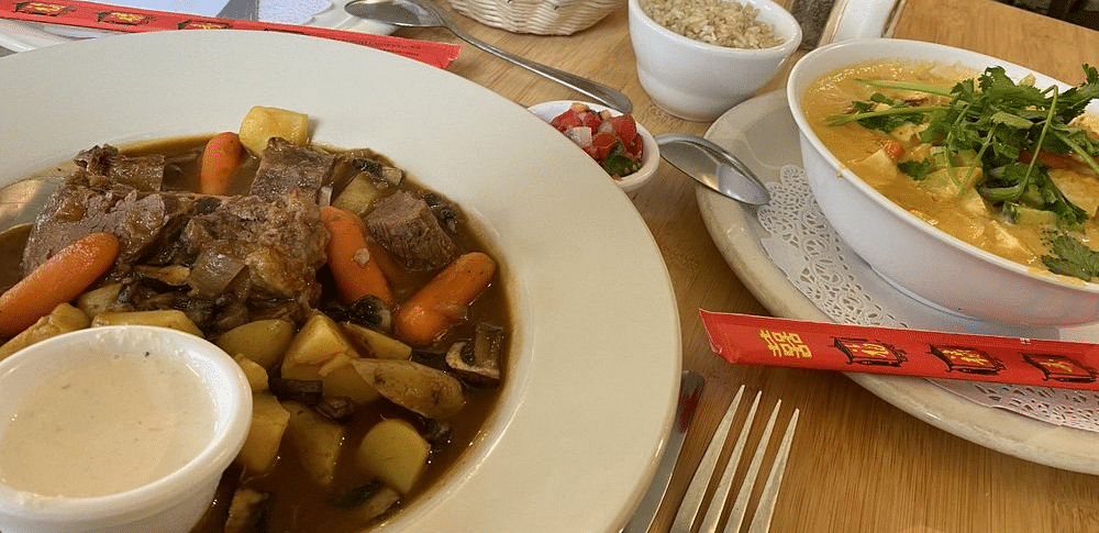 A table setting with a bowl of salad, a basket of bread, and a bowl of stew with meat, potatoes, and carrots.