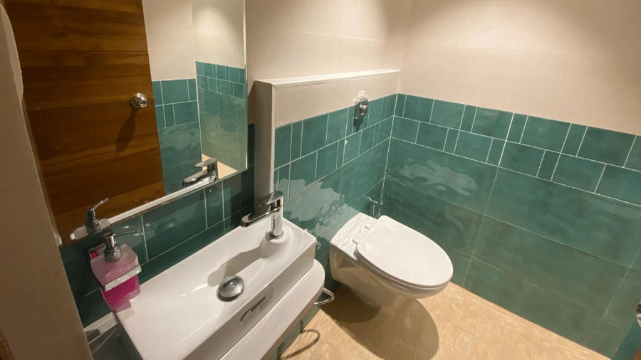 Clean and modern restroom featuring teal wall tiles, a white ceramic sink, and a large vanity mirror - DAN Resorts & Weddings, Palghar