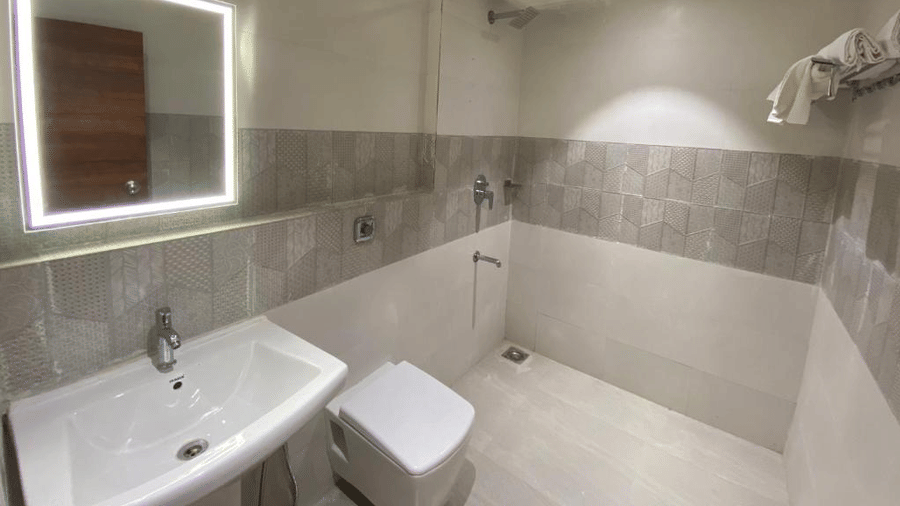 Contemporary bathroom featuring a glowing LED vanity mirror, white porcelain sink, and walk-in shower area - DAN Resorts & Weddings, Palghar