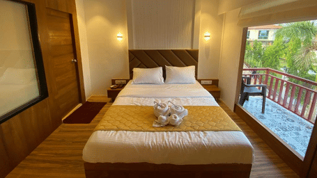Well-lit luxury room featuring a king size bed and large glass doors leading to a private wooden balcony - DAN Resorts & Weddings, Palghar