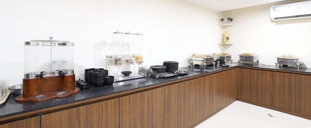 A wide-angle shot of the buffet counter at Aranaya Restaurant at Pravasa Stay, Ahmedabad (Alba Premier), with wooden panels covering the bottom of the counter. 