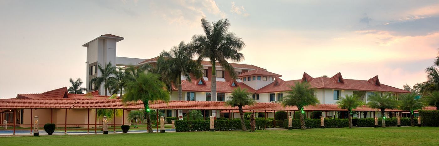 Exterior view showcasing lush grass and palm trees encircling the resort under a partly cloudy sky  | Crescent Spa & Resorts