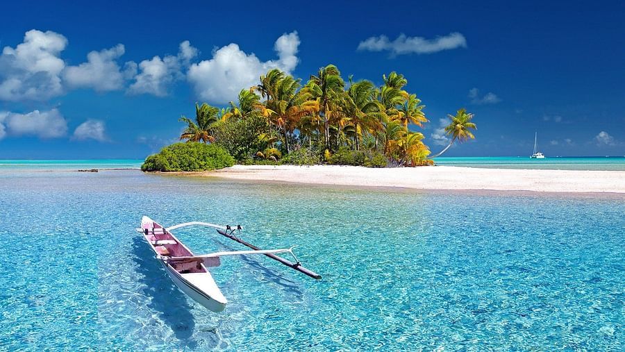 a canoe sailing towards an island with brown sand and blue sky in the background