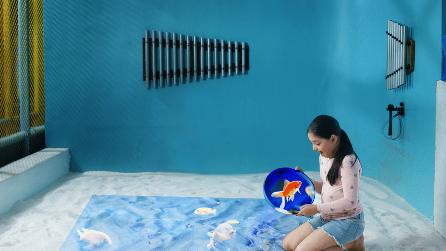 A young girl interacts with a digital projection of swimming fish inside an interactive sensory sandpit room at Tic Tac Tot.