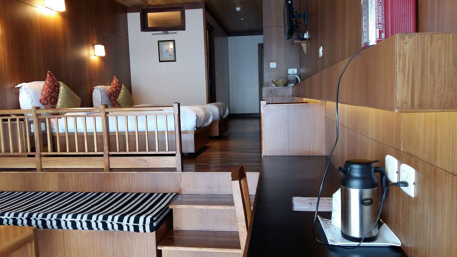The double bed in the Deluxe room placed on an elevated platform from the living area that has a table and tea and coffee maker at Cedar Inn in Darjeeling.