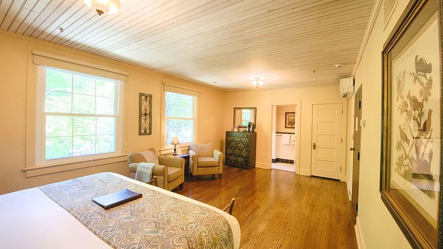 a brightly lit bedroom featuring a double bed with a file kept over it and with a comfortable seating area in front of it - Historic Tapoco Lodge