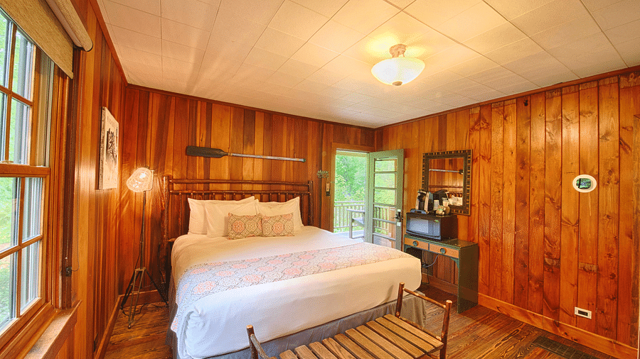 front view image of a cozy double bed in a room with wooden walls and flooring with a small chandelier - Historic Tapoco Lodge