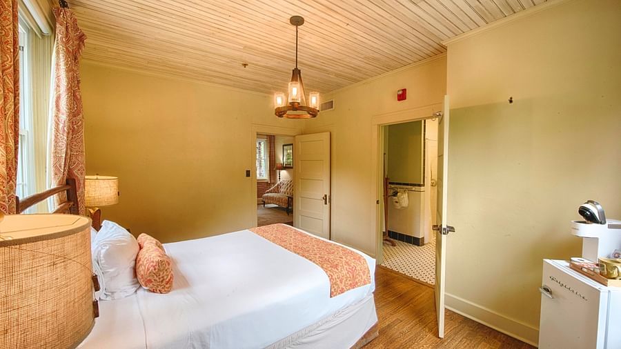 a room with two door along with a double bed and a chandelier hanging over ita brightly lit bathroom featuring a door opening to the bedroom overlooking the double bed - Historic Tapoco Lodge