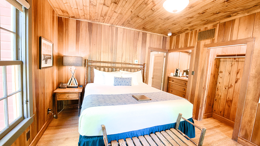 a bedroom featuring a a plush double bed with a window besides it and a small sitting bench in front of the bed - Historic Tapoco Lodge