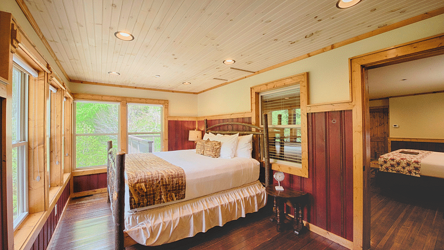 corner view image of a double bed overlooking amazing lush green views from the huge windows in front of it - Historic Tapoco Lodge