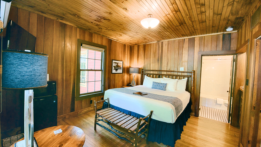 a wide angle shot of a bedroom with a modern looking table lamp kept on the round wooden coffee table - Historic Tapoco Lodge
