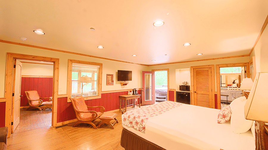 a double bed placed in front of a cushioned armchair that is besides a door frame leading to the other bedroom - Historic Tapoco Lodge