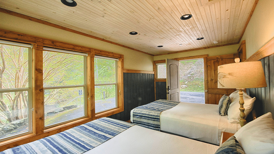 two double beds facing towards the huge windows with lush green forest views and a door opening to the exterior - Historic Tapoco Lodge