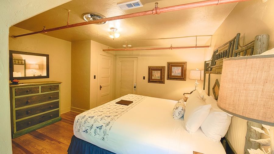 corner view image of the bedroom with two wide framed photos wall mounted in the corner and a wooden drawer in front of the bed - Historic Tapoco Lodge